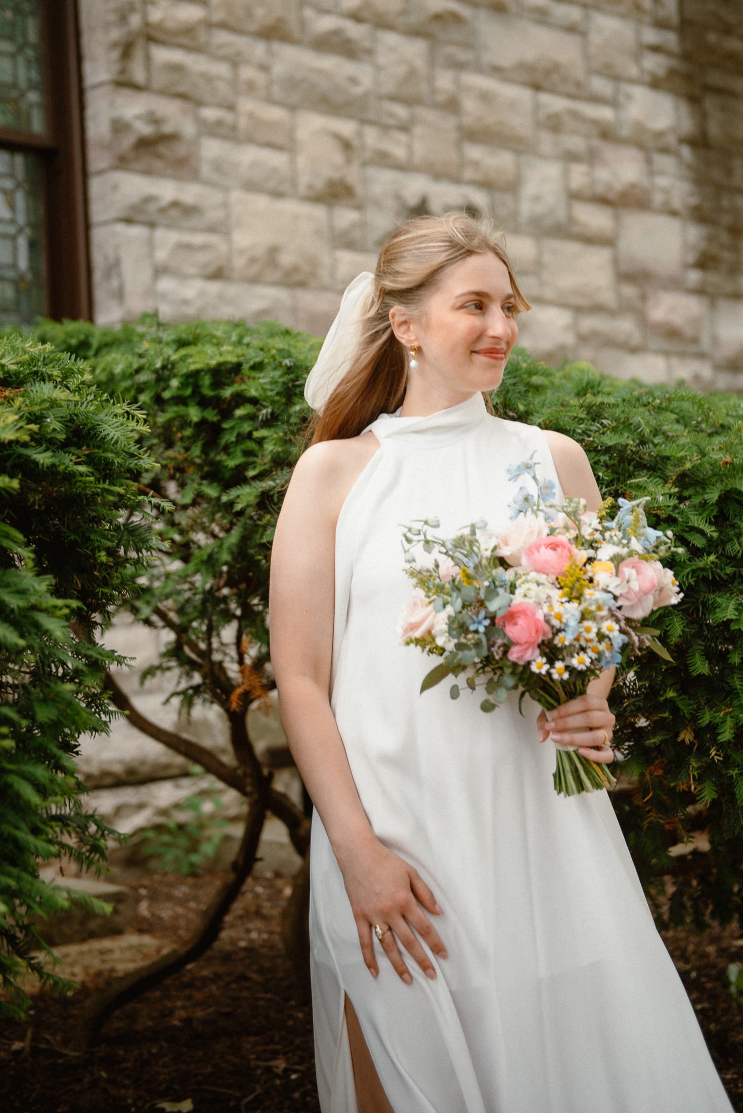 Relaxed portrait of bride outside of Eaton Chapel in Beloit holding a colorful spring inspired bouquet made by Blooms by Brandi.