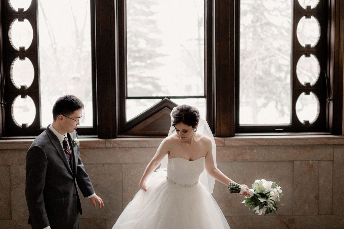 Bride adjusting wedding gown in front of large window