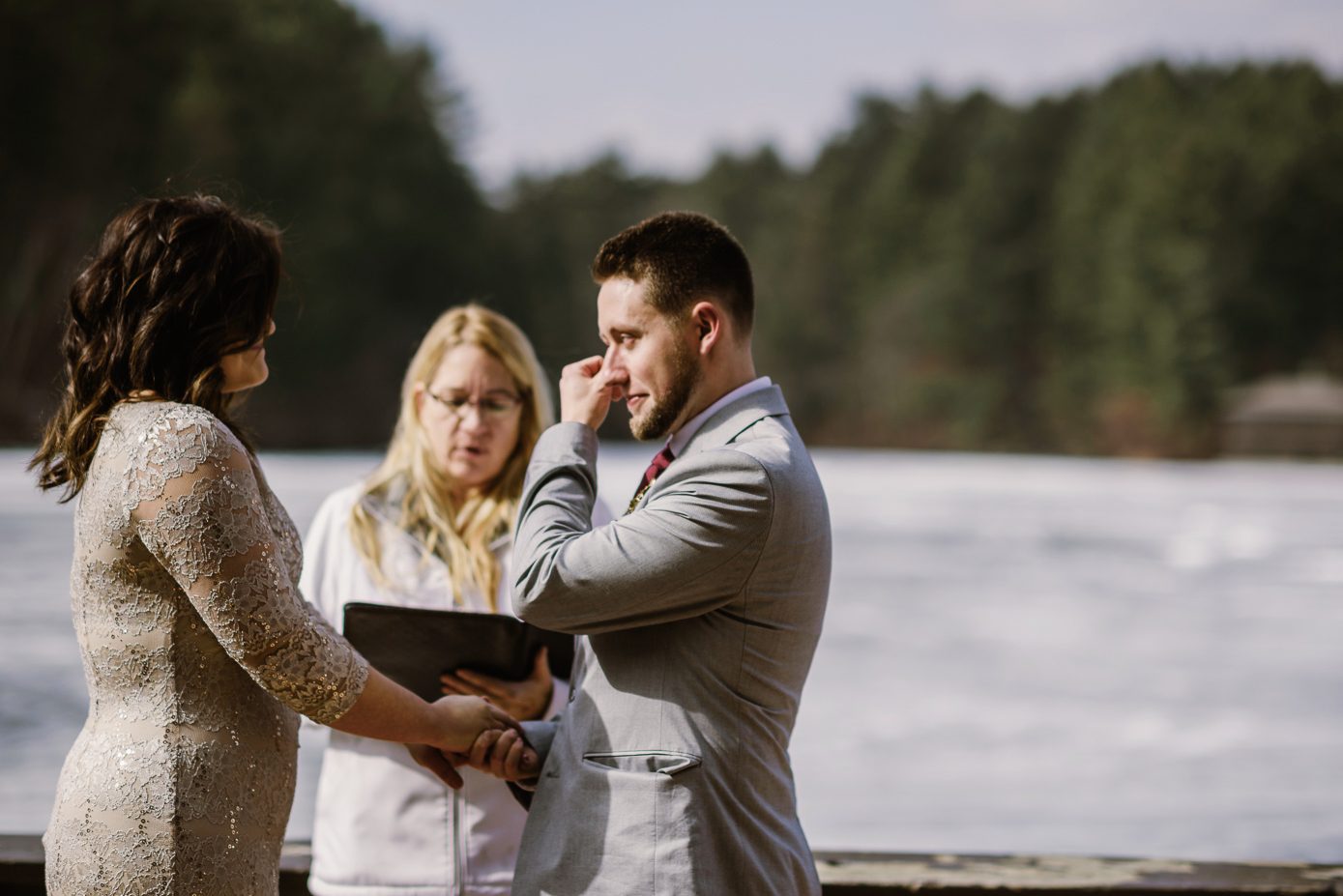Groom wiping tear during wedding ceremony on Mirror Lake.