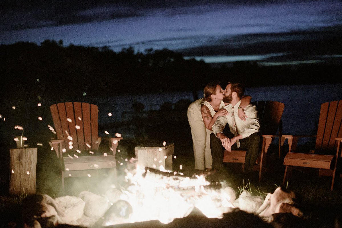 Bride and groom kiss in front of campfire.